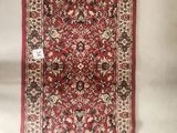 a red rug hanging on a wall next to a white wall