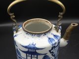 blue and white porcelain teapot with brass handle on black background