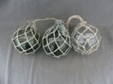 trois boules de Noël en verre vert suspendues à une ficelle sur un tissu blanc