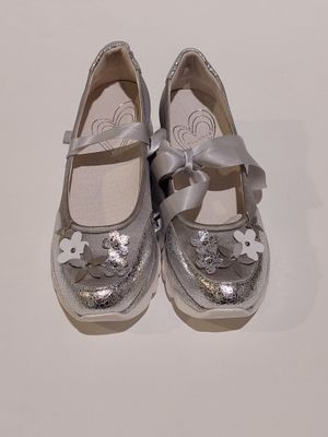 une paire de chaussures argentées ornées de nœuds, posées sur un fond blanc