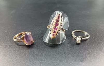 three rings and a ring with a pink stone on a black surface