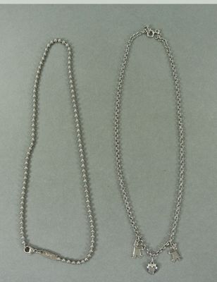 deux colliers en argent posés sur une surface grise, avec une chaîne en argent