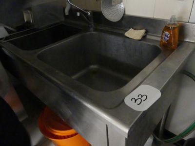 un évier en acier inoxydable dans une cuisine, sur lequel est accrochée une pancarte