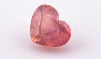 un gros plan d'une pierre rose en forme de cœur posée sur une surface blanche