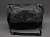 le sac à main noir est posé sur une surface grise, entouré d'une chaîne
