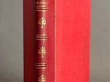 an old red book sitting on top of a table next to a gray wall