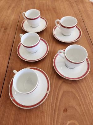 six cups and saucers sitting on a wooden table with red rims