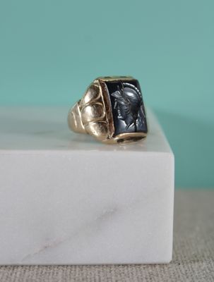 an image of a gold and black stone ring on a white marble block