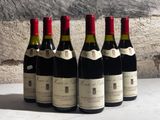 six bottles of wine are lined up on a table in front of a stone wall