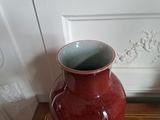 a red vase sitting on a wooden table in front of a white door