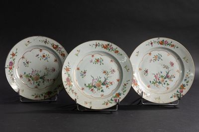 trois assiettes ornées de motifs floraux sont disposées sur un présentoir, sur fond noir