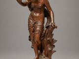 une statue antique en bronze représentant une femme tenant un oiseau, posée sur un socle