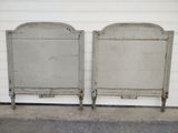 two metal beds sitting next to each other in front of a white wall