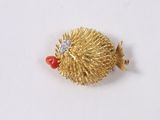 a gold hedgehog brooch with a red bead on it