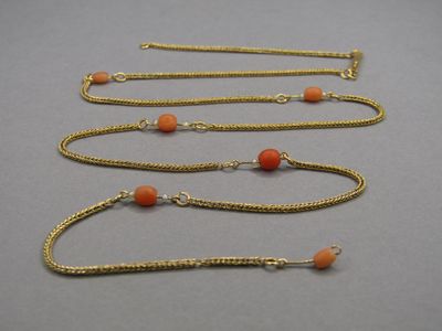 three gold chain necklaces with orange beads on a gray surface