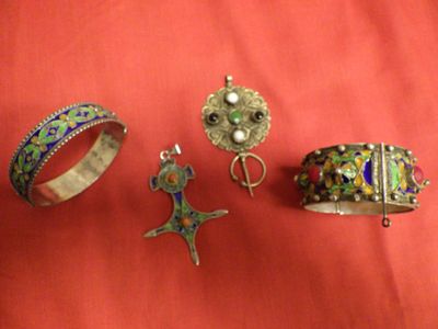 trois bijoux en argent et en émail posés sur un tissu rouge