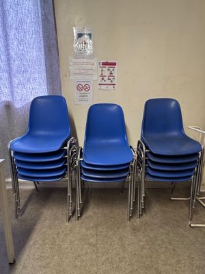 Quatre chaises bleues sont alignées contre un mur dans une salle d'attente