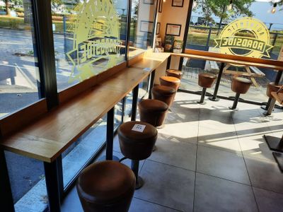des tables et des tabourets devant une fenêtre où est accrochée une pancarte indiquant « limonade »