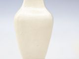 a small white vase on a wooden stand on a white surface