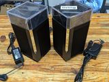 two speakers sitting on a wooden table with a charger