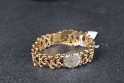un bracelet en or avec une montre posée sur une surface noire, à côté d'un téléphone portable