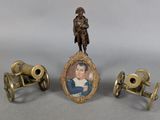 three miniature objects including a miniature cannon, a miniature picture frame and a miniature picture of a man