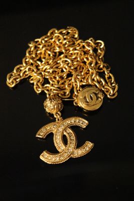 a close up of a gold chain with a chanel charm on it