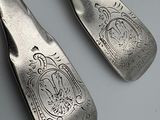 two silver spoons with designs on them sitting on a table
