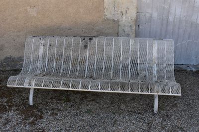 a white metal bench sitting in front of a wall