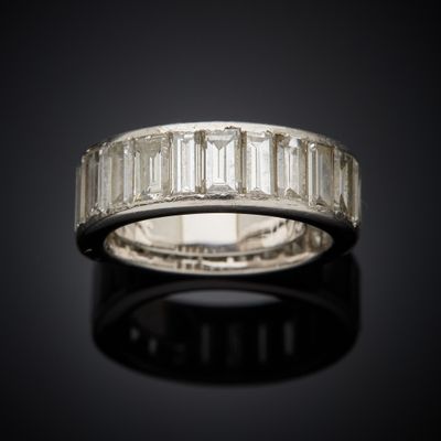 a white gold ring with baguets of diamonds on a black surface