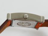 someone is holding a watch with a brown strap on a white surface