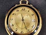 une montre de poche en or avec un cadran noir, posée sur un tissu noir