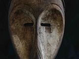un vieux masque en bois posé sur un socle, sur fond noir