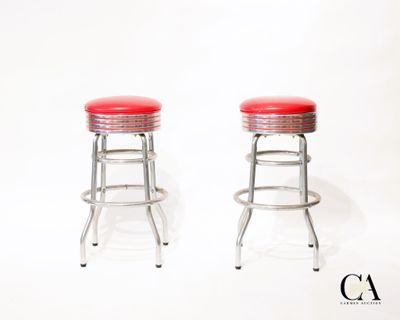 une paire de tabourets chromés avec des assises rembourrées rouges sur fond blanc