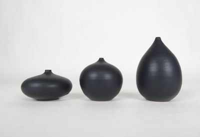 trois vases noirs posés les uns à côté des autres sur une surface blanche