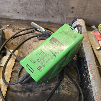 a green power supply sitting on the floor next to a pile of tools