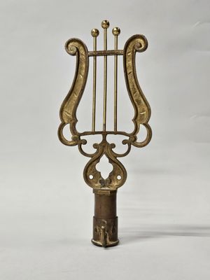 une harpe ancienne en laiton posée sur un support, sur fond blanc