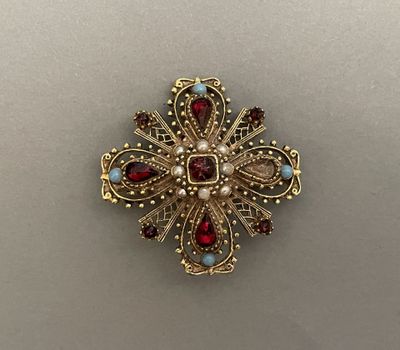 a close up of a gold broochle with red and white stones