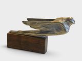une image représentant une statue d'oiseau en bronze posée sur un socle en bois