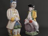 two ceramic figurines of a man and a woman sitting on a barrel