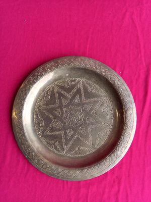 a silver plate with a design on it on a pink surface