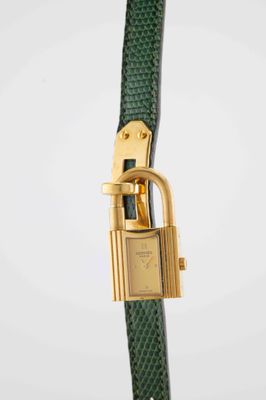 a close up of a watch with a green strap and gold clasp