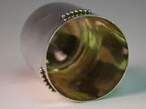 a close up of a silver vase with a green swirl
