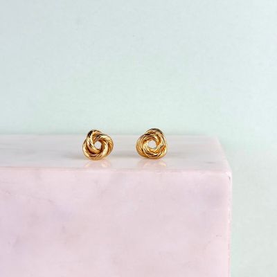 une paire de boucles d'oreilles en or posée sur un bloc de marbre