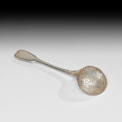 une cuillère en argent ancienne posée sur une surface blanche avec un fond noir