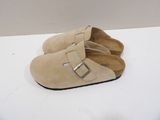beige sued mulers with buckles on the front and a black sole