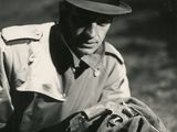 photo en noir et blanc d'un homme vêtu d'un trench-coat et d'un chapeau, tenant un gant de baseball