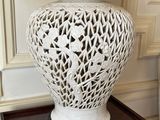 a white vase on a table with a lamp on top of it