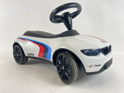 voiture jouet à conducteur assis de style BMW blanche, avec des roues noires et des rayures rouges, blanches et bleues