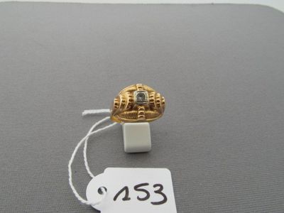 une bague en or sertie d'un diamant, posée sur une surface grise